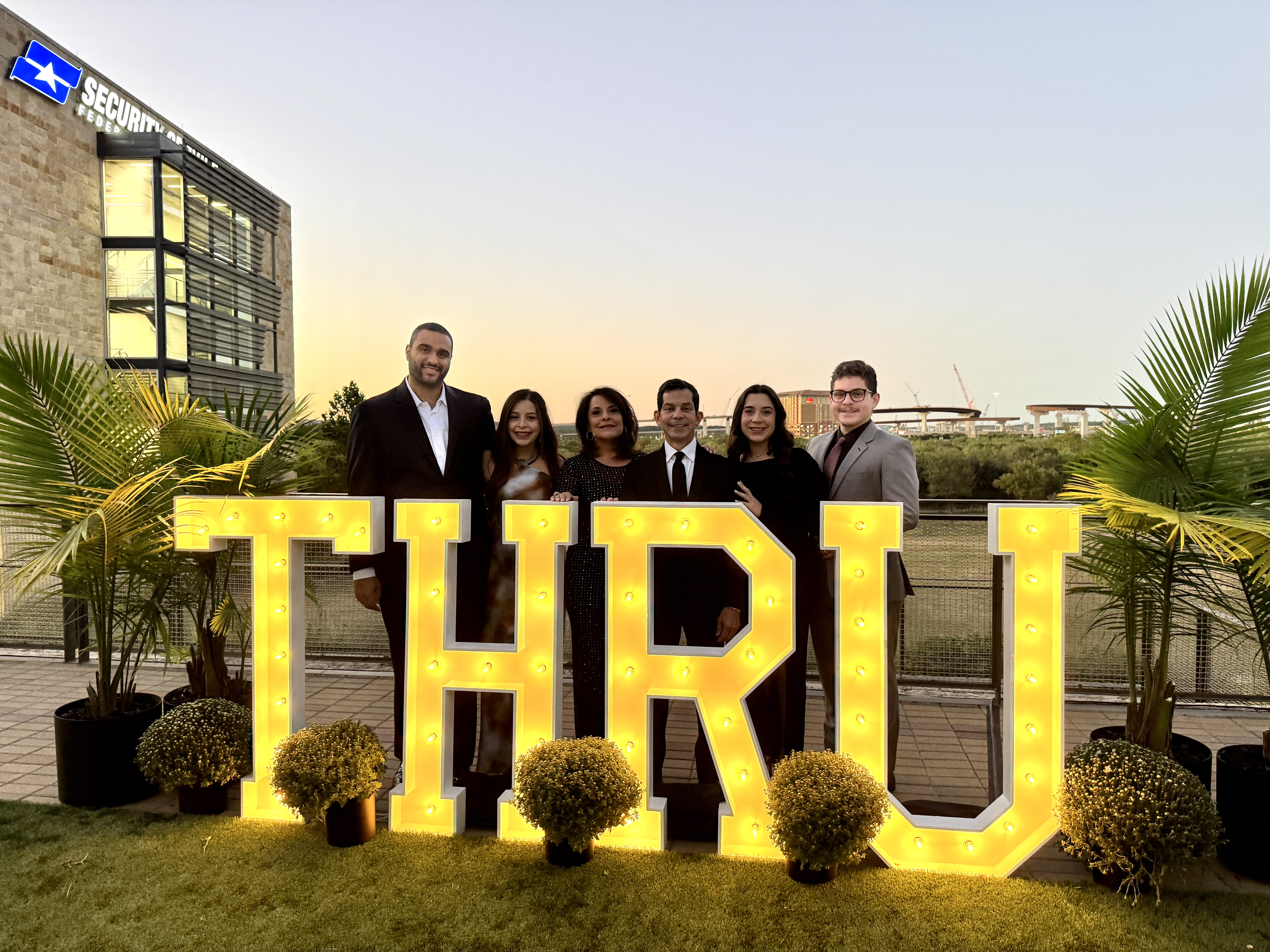 The Garza family beside the illuminated THRU sign at sunset